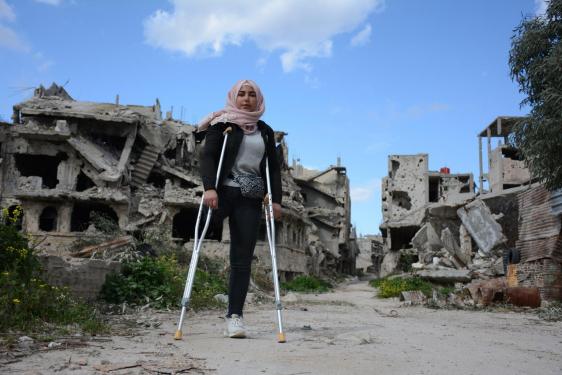 A young woman using crutches in front of a destroyed building in Syria