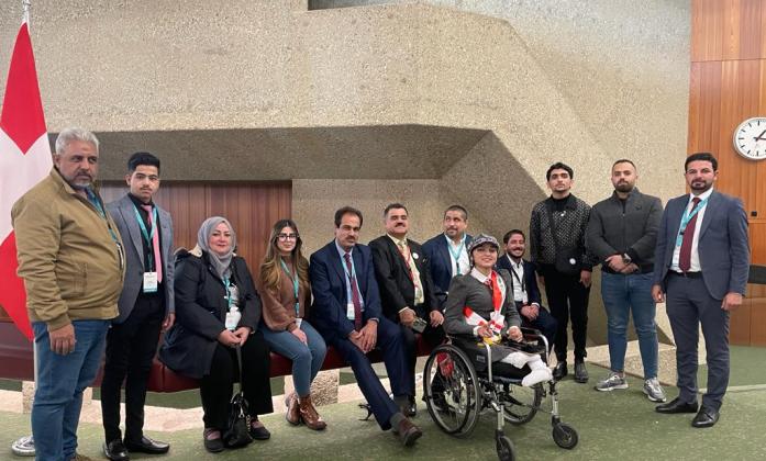 Jose Viera with the delegation of persons with disabilities from Iraq. There are a few people who are sitting on a bench and some standing on either side. There is a wheelchair user in the front.