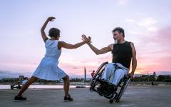 A man in a wheelchair dances with a woman on the beach